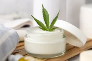 A close-up image of a container of cannabis topical ointment with a cannabis leaf in it.